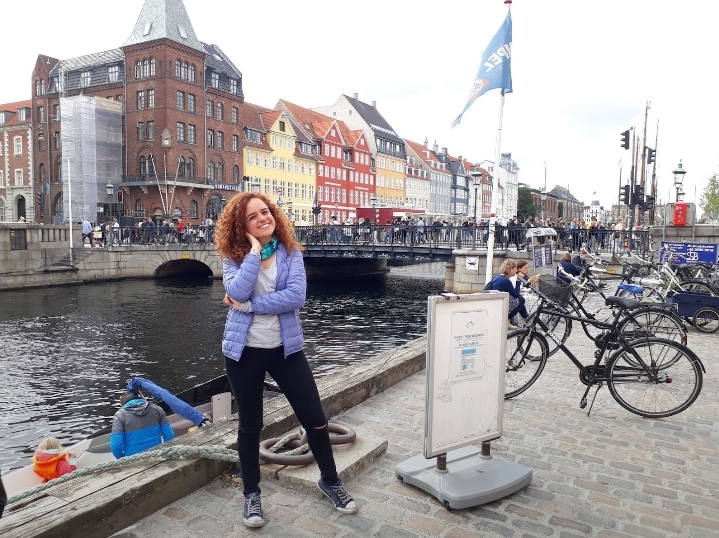 Woman with curly hair standing in front of a canal and building in Copenhagen